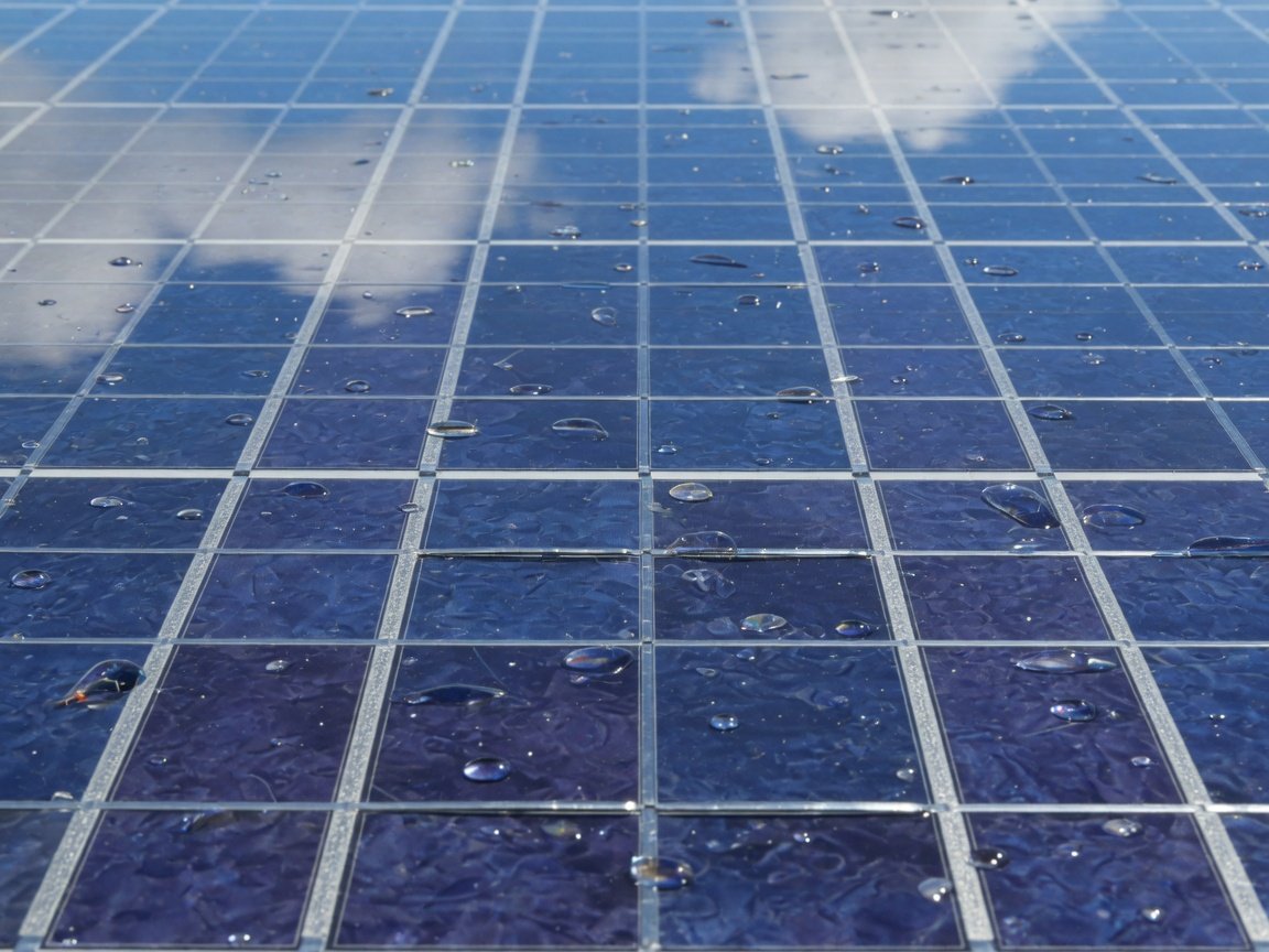 Close de células fotovoltaicas de silício com reflexo do céu e gotas de água